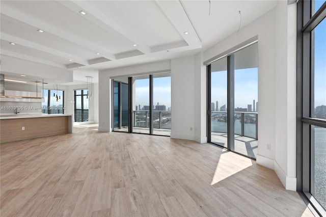 unfurnished living room featuring light wood-style floors, baseboards, a city view, and beamed ceiling