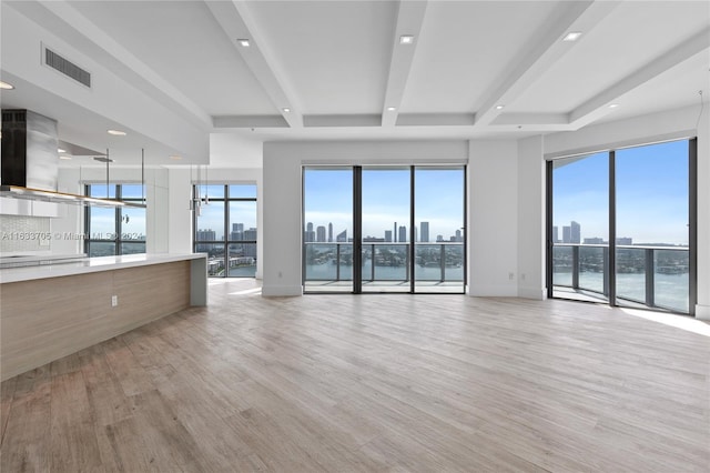 unfurnished living room featuring visible vents, baseboards, light wood-style floors, beam ceiling, and a view of city