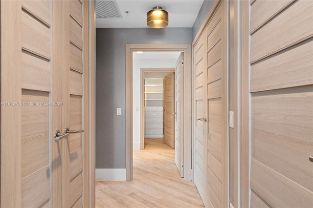 hall featuring light wood-style floors, baseboards, and visible vents