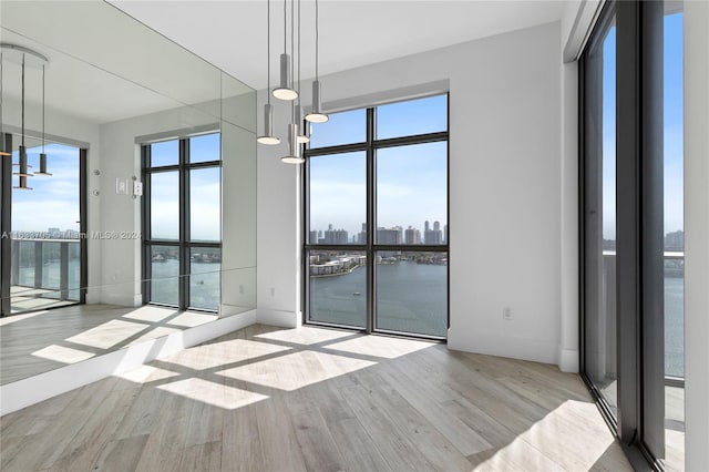 spare room featuring baseboards, light wood-type flooring, a water view, and a city view