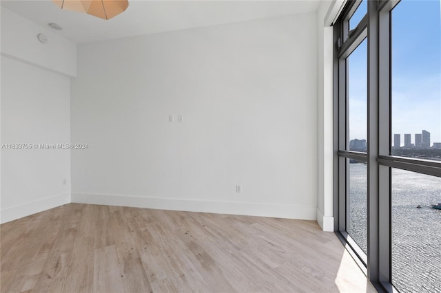 unfurnished room featuring light wood-style floors, a view of city, and baseboards