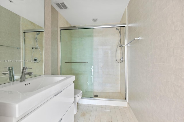 bathroom with visible vents, toilet, vanity, a shower stall, and tile walls