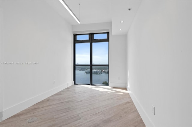 unfurnished room featuring a water view, light wood-style floors, attic access, and baseboards