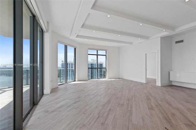 spare room with light wood-type flooring, visible vents, beamed ceiling, and baseboards