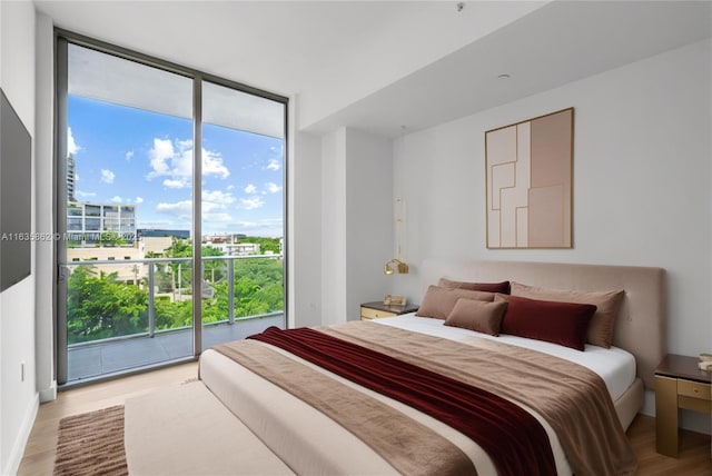 bedroom with access to outside, light wood-type flooring, and a wall of windows