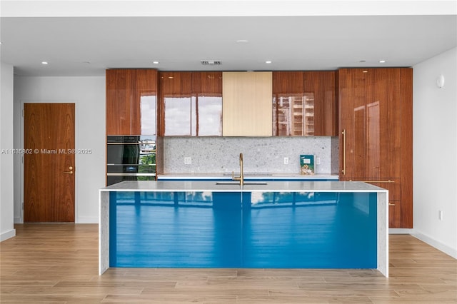 kitchen featuring sink, an island with sink, and light hardwood / wood-style flooring