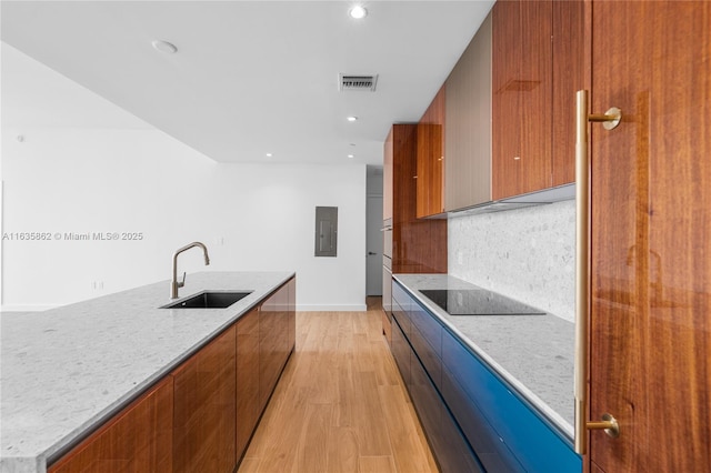 kitchen with light stone countertops, sink, electric panel, light hardwood / wood-style floors, and black electric cooktop