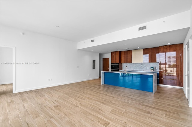 kitchen with decorative backsplash, oven, light wood-type flooring, and a kitchen island with sink