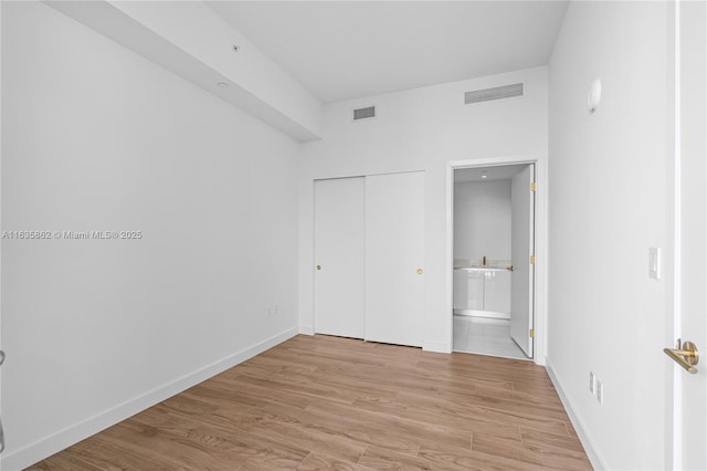 unfurnished bedroom featuring a closet, light wood-type flooring, and ensuite bath