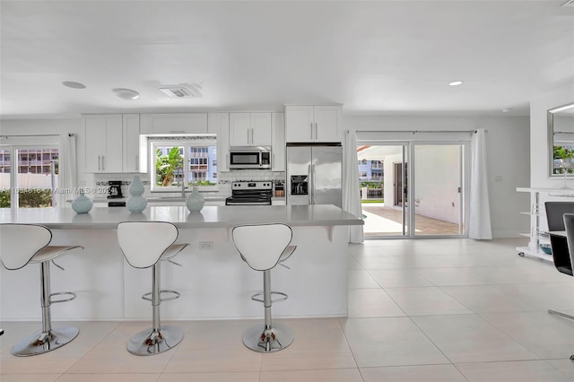 kitchen with light tile patterned flooring, white cabinetry, a center island, and stainless steel fridge