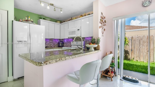 kitchen with white appliances, kitchen peninsula, decorative backsplash, stone countertops, and white cabinetry