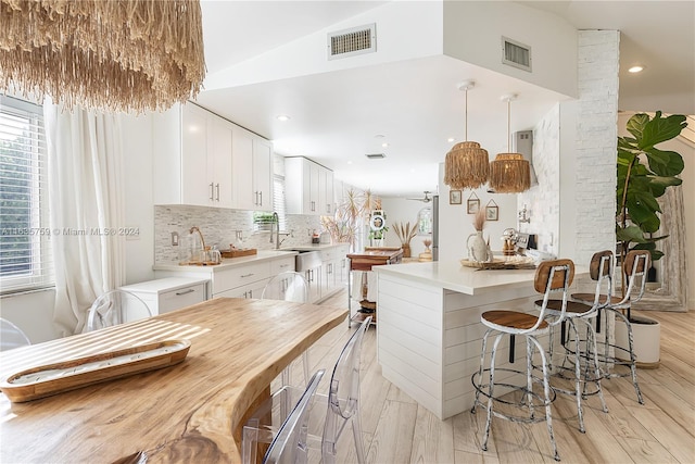 kitchen featuring lofted ceiling, backsplash, a center island, white cabinetry, and light hardwood / wood-style floors