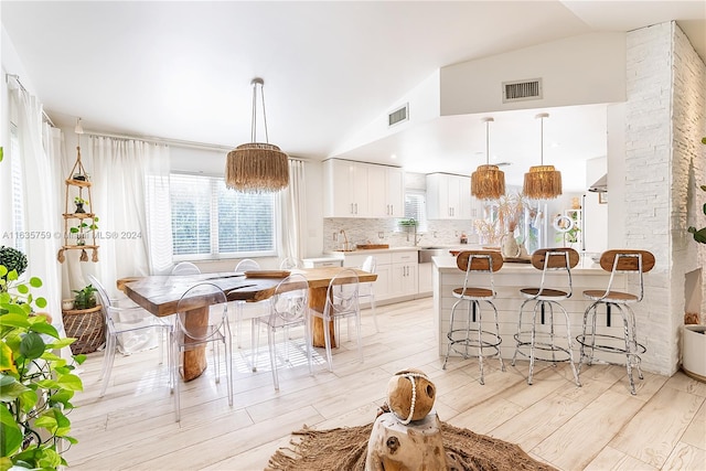 dining area featuring sink, vaulted ceiling, and light wood-type flooring