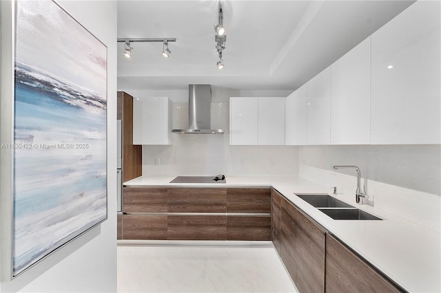 kitchen with white cabinets, wall chimney range hood, black electric stovetop, sink, and backsplash