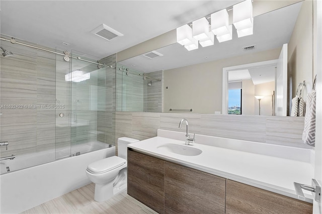 full bathroom with toilet, vanity, tile walls, backsplash, and enclosed tub / shower combo