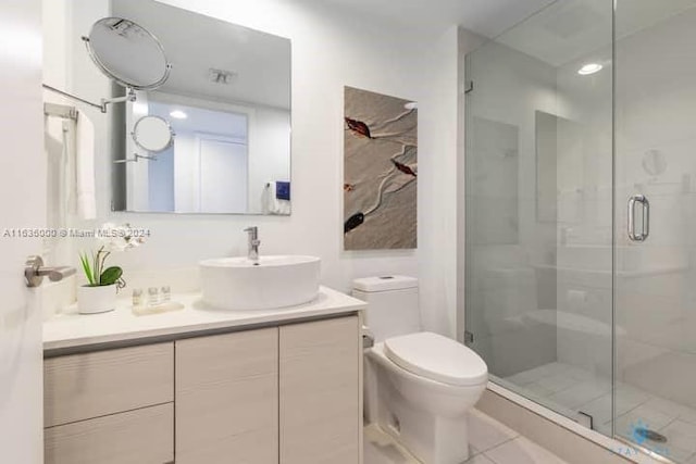 bathroom with a shower with shower door, vanity, tile patterned flooring, and toilet