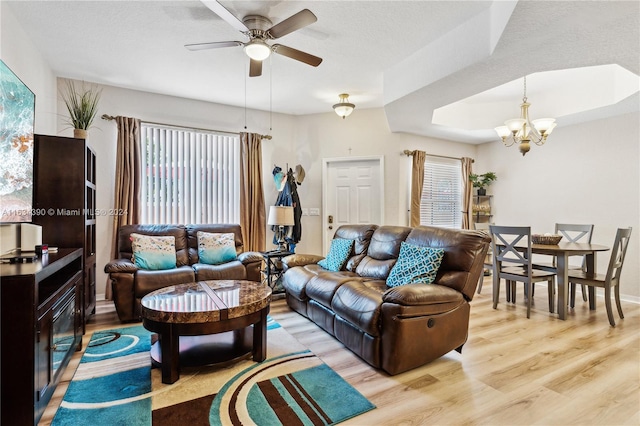 living area featuring ceiling fan with notable chandelier, a tray ceiling, light wood finished floors, and a textured ceiling