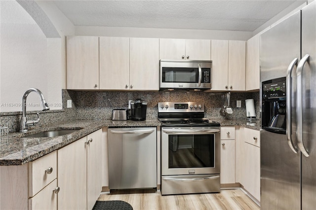 kitchen with stainless steel appliances, dark stone countertops, a sink, and decorative backsplash