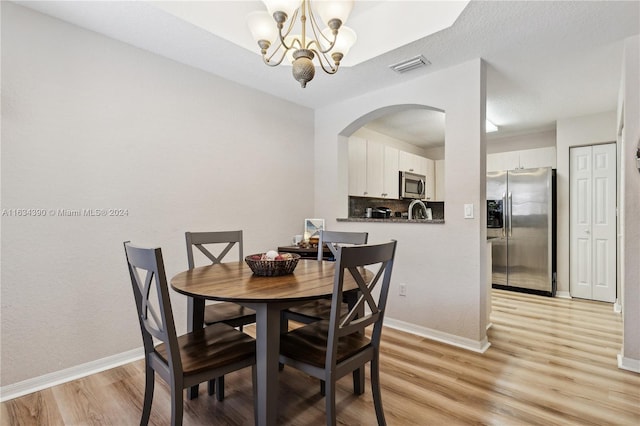 dining area featuring arched walkways, visible vents, baseboards, light wood-type flooring, and an inviting chandelier