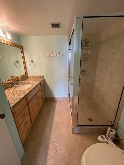 bathroom with a shower with shower door, toilet, vanity, and tile patterned floors