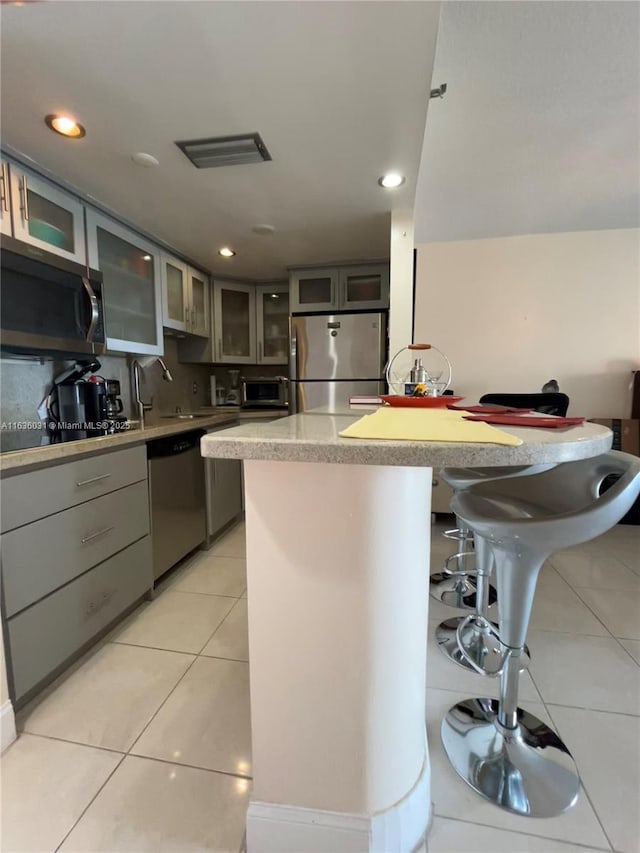 kitchen featuring gray cabinets, appliances with stainless steel finishes, a breakfast bar, backsplash, and light tile patterned floors