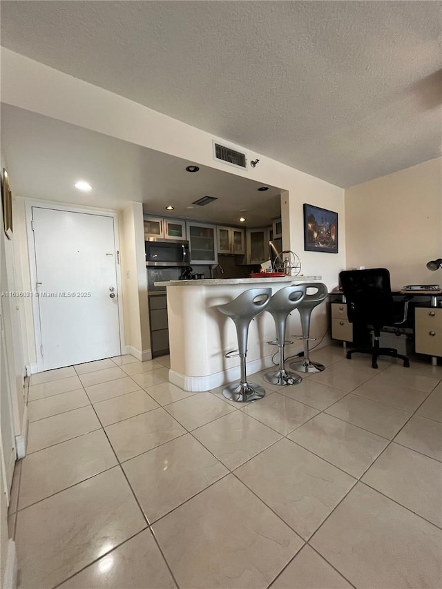 kitchen with a breakfast bar, light tile patterned floors, a textured ceiling, and kitchen peninsula