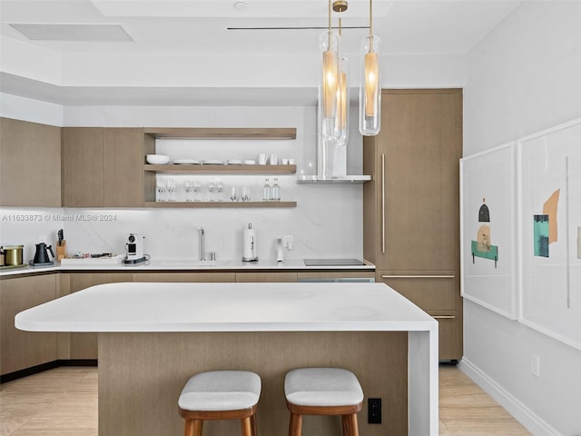 kitchen with black electric stovetop, sink, light hardwood / wood-style flooring, decorative light fixtures, and a kitchen bar