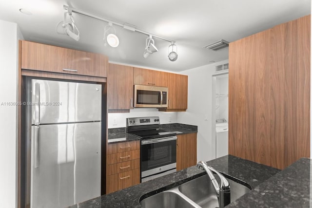 kitchen with appliances with stainless steel finishes, sink, and dark stone countertops