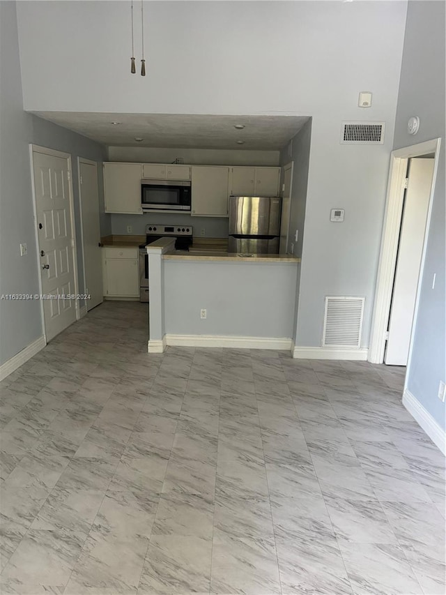 interior space featuring appliances with stainless steel finishes, light tile patterned flooring, kitchen peninsula, and a towering ceiling