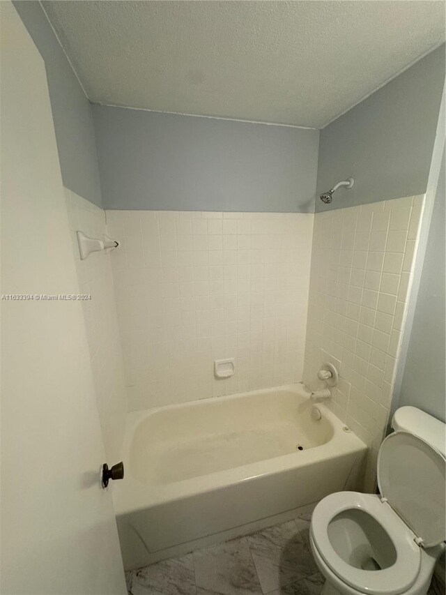 bathroom with tile patterned flooring, tiled shower / bath combo, toilet, and a textured ceiling