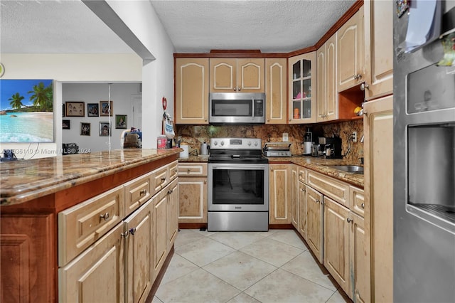 kitchen with appliances with stainless steel finishes, tasteful backsplash, light stone counters, kitchen peninsula, and light tile patterned flooring