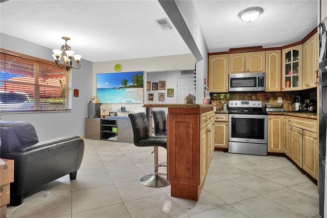 kitchen with light tile patterned flooring, a chandelier, stainless steel appliances, decorative backsplash, and a kitchen bar