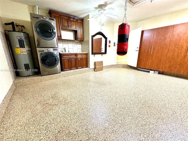 clothes washing area featuring cabinets, a textured ceiling, ceiling fan, water heater, and stacked washer / dryer