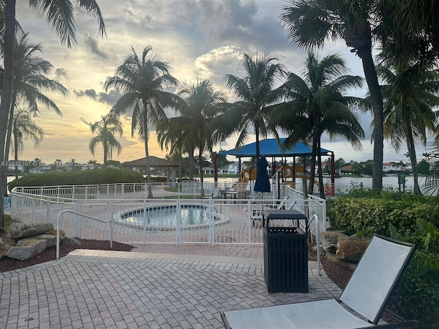 pool at dusk featuring a playground and a water view