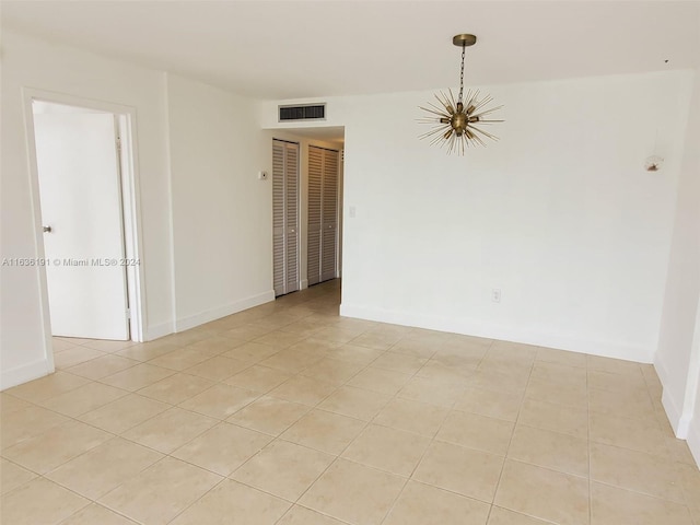 empty room with a notable chandelier and light tile patterned floors