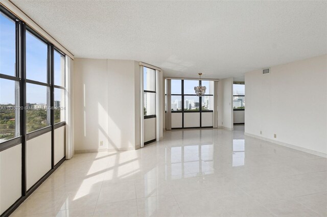 tiled empty room featuring floor to ceiling windows, a notable chandelier, and a textured ceiling