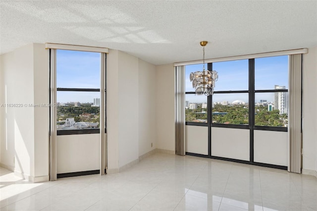 tiled empty room with plenty of natural light, a textured ceiling, and a notable chandelier