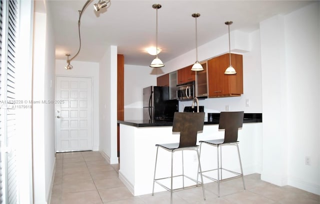 kitchen featuring a peninsula, stainless steel microwave, dark countertops, brown cabinets, and freestanding refrigerator