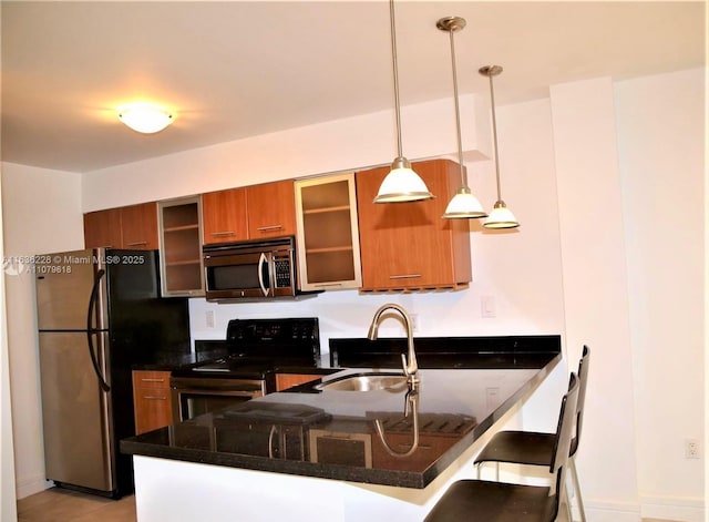 kitchen featuring a kitchen breakfast bar, stainless steel appliances, a sink, a peninsula, and brown cabinets