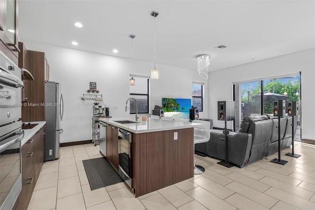 kitchen featuring dark brown cabinets, an island with sink, sink, appliances with stainless steel finishes, and light tile patterned floors