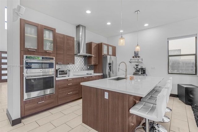 kitchen featuring a breakfast bar area, tasteful backsplash, stainless steel appliances, a kitchen island with sink, and wall chimney exhaust hood