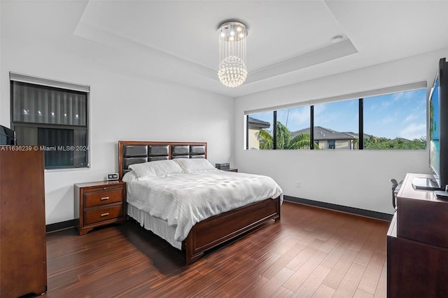 bedroom with an inviting chandelier, dark wood-type flooring, and a tray ceiling