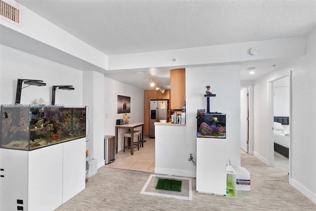 interior space featuring stainless steel fridge with ice dispenser, a textured ceiling, light colored carpet, and rail lighting