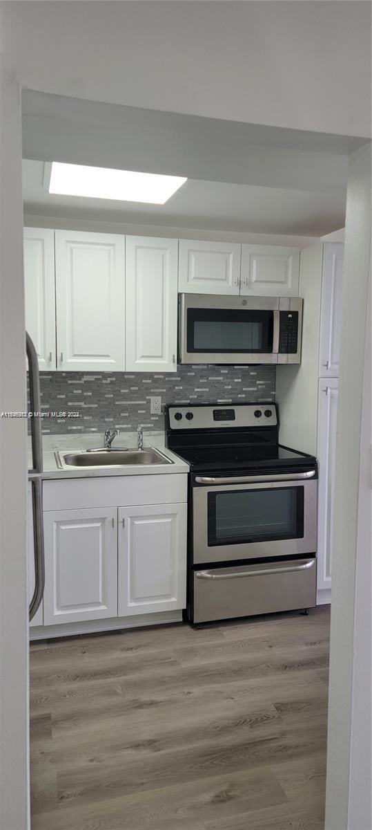 kitchen with sink, appliances with stainless steel finishes, light hardwood / wood-style floors, and white cabinetry