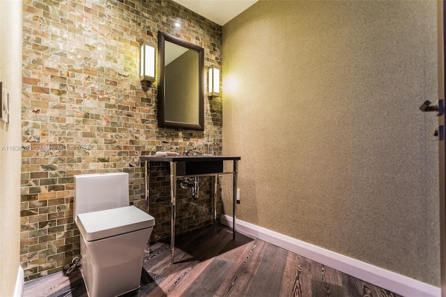 bathroom featuring wood-type flooring, toilet, and brick wall