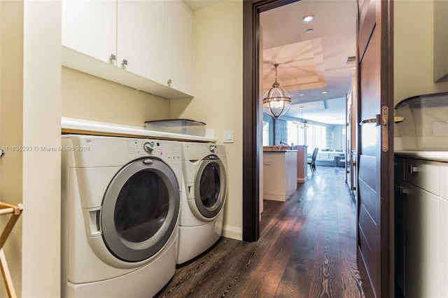 clothes washing area featuring washing machine and clothes dryer, a chandelier, dark hardwood / wood-style flooring, and cabinets