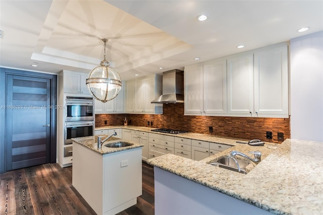 kitchen featuring decorative light fixtures, light stone counters, wall chimney range hood, and sink