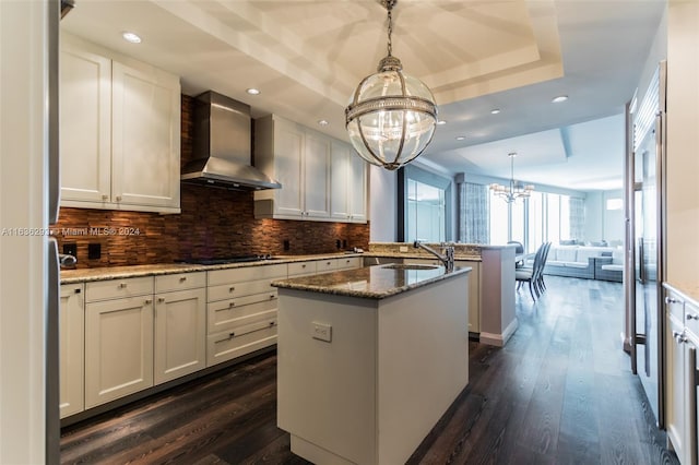 kitchen featuring wall chimney exhaust hood, dark wood-type flooring, hanging light fixtures, dark stone counters, and a kitchen island