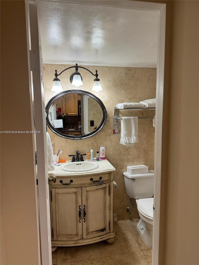 bathroom featuring tile patterned flooring, tile walls, a textured ceiling, toilet, and vanity