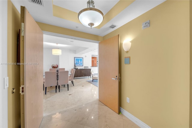 corridor featuring a raised ceiling and light tile patterned floors